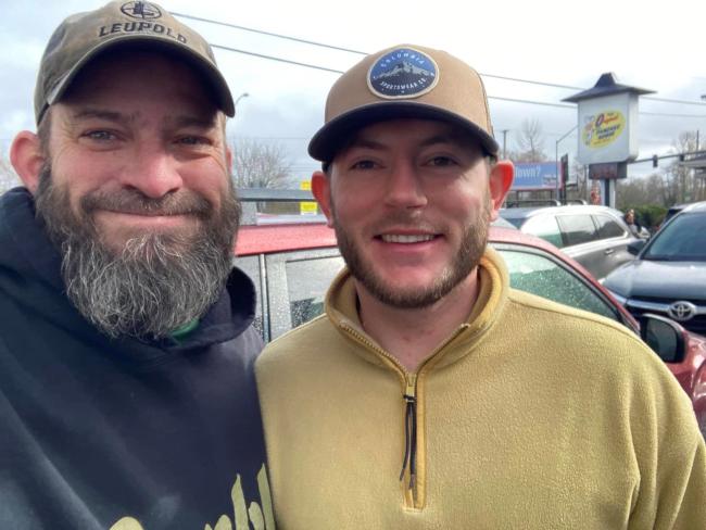 Two men in baseball caps stand shoulder to shoulder and smile