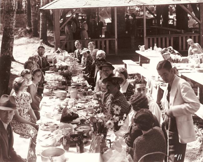 A historic sepia toned photo of families at a picnic table outdoors
