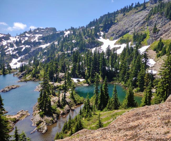 A scenic photo of a series of lakes in a bowl with some snow and blue sky.