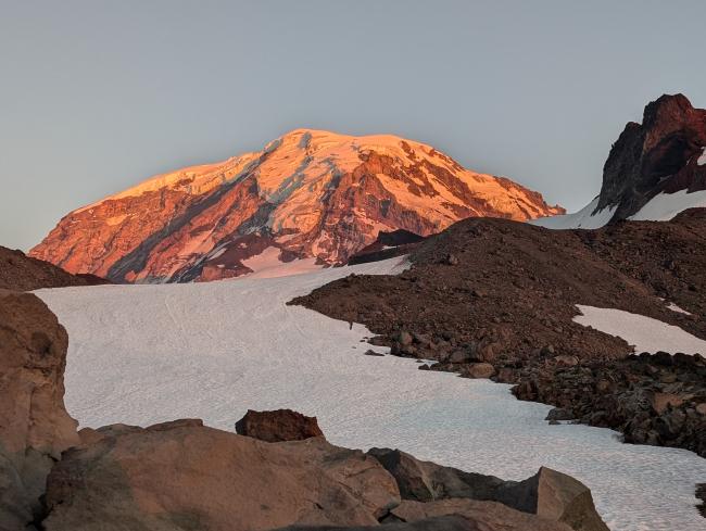 Mount Rainier with sunset alpenglow from behind a ridge.