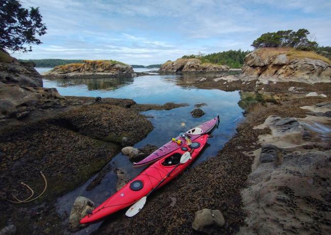 A red kayak beached in a sandstone cove with glassy water.