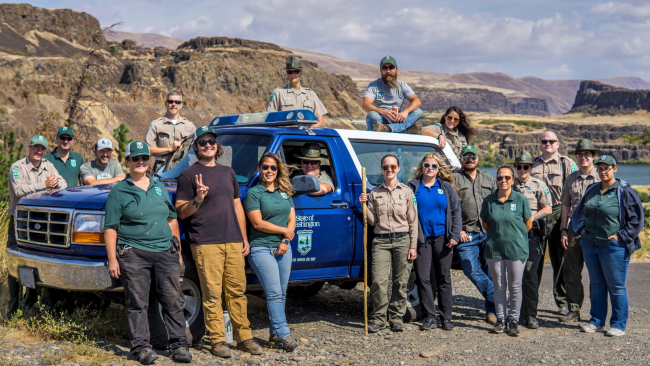 A group of staff around a ranger truck with brown bluffs in the background.