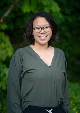 Janette Chien, Diversity, Equity and Inclusion Director for Washington State Parks poses in front of evergreens. 