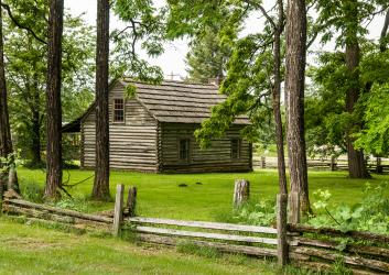 old world cabin of wood surrounded by green grass and wood rail fence