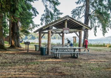 round log picnic shelter with tables , bbq grill and trash cans 