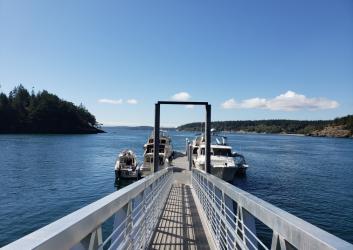 Looking down the dock at James Island. There are boats moored on either side. It is sunny and there are green islands in the distance.