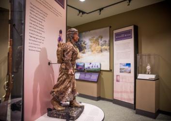 Inside the Interpretive Center, a small statue of Sacajawea sits on a podium with a narrative of the history of the Lewis and Clark Trail journey behind her. Other displays can be seen in the background.