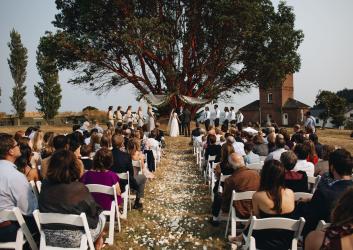 Outdoor wedding at Fort Worden State Park in front of a madrona tree and castle.