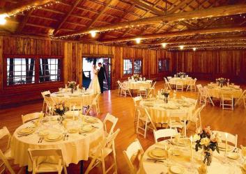 A couple stands by the door of a log cabin with the interior set for a wedding in golden light.