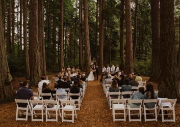 A couple getting married in a forest setting with wedding attendees sitting in rows of chairs