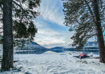 Red tent in a snowy campsite near a lake with mountains in the distance