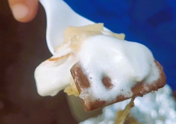 Person holds out a spoon with banana, chocolate and marshmallow