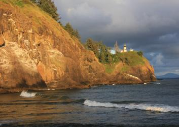 sunlit cliffs with lighthouse above ocean waves