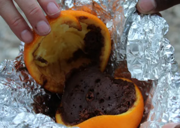 A halfed orange in tin foil. The orange top of the orange is pulled back and there's chocolate cake inside the rind.