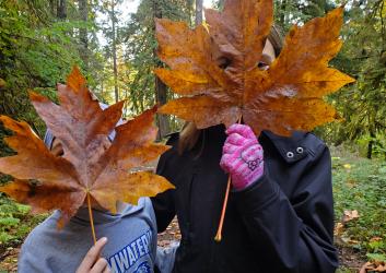 An adult and child with their faces covered by bigleaf maple leaves.