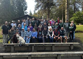 A group of people sit for a photo in front of trees.