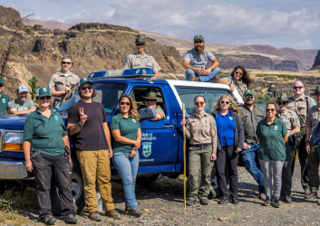 A group of staff around a ranger truck with brown bluffs in the background.