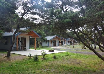 A row of white and blue cabins in a field with trees.