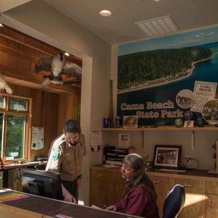 Two employees working at the contact station where Discover passes can be purchased and you can check-into cabins. The building is rustic with lots of exposed wood. There are some taxidermy birds handing from the ceiling. Three are visible from this angle. 