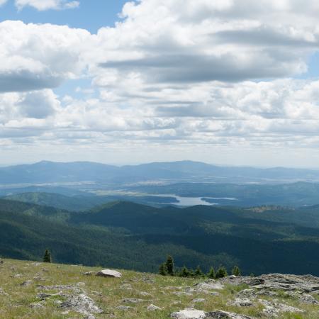 The expansive view from the summit of Mount Spokane with partially cloudy skies, a lake, and hills and mountains in the distance.