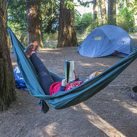Campsite with pitched tent and hammock occupied by someone reading a book
