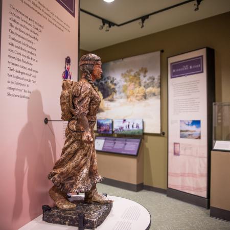 Inside the Interpretive Center, a small statue of Sacajawea sits on a podium with a narrative of the history of the Lewis and Clark Trail journey behind her. Other displays can be seen in the background.