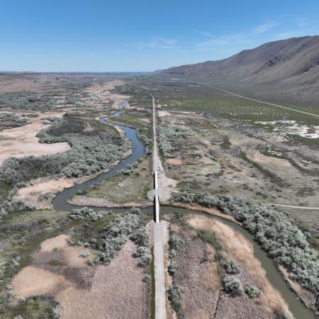 A clear sky aerial view of two trestles connecting a gravel trail over a creek.