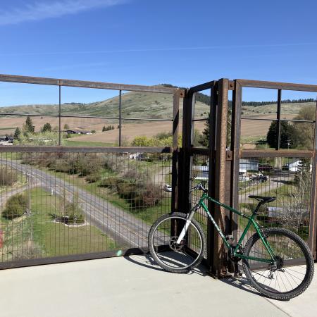 A bicycle is leaned against a safety fence on a bridge over a road. The view looks out over a few houses with a small mountain in the background