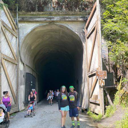 A couple smiles in front of a tunnel entrance where several other people are walking in and out