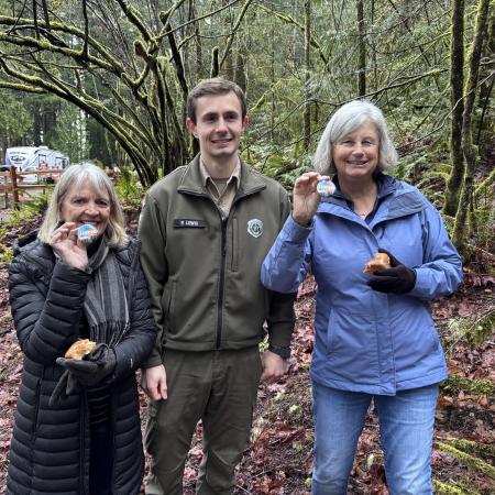 Two female hikers standing with Ranger Lewis holding up their First Day Hike Buttons