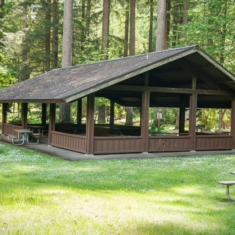 Covered kitchen shelter surrounded by a grassy field and a couple picnic tables at Battle Ground Lake State Park. 