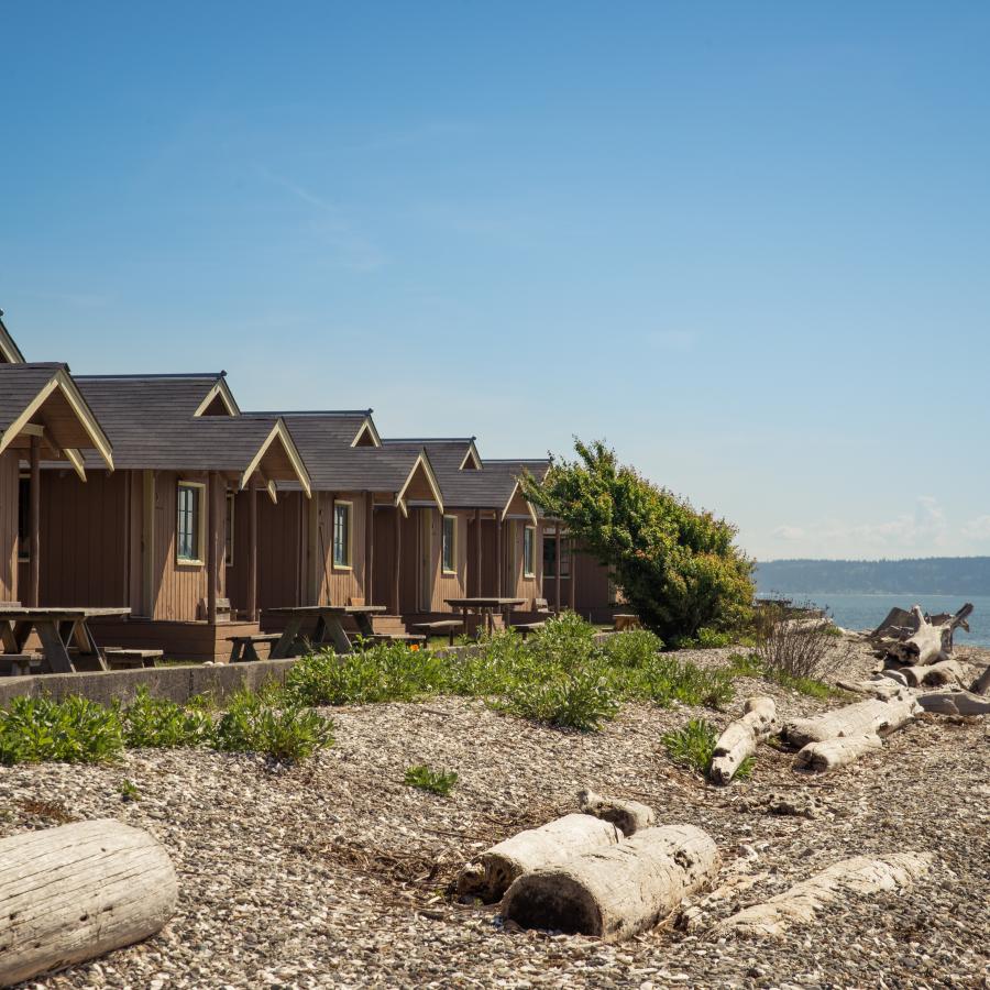 multiple beachfront cabins at Cama beach state park with the beach visible with rocks and driftwood.