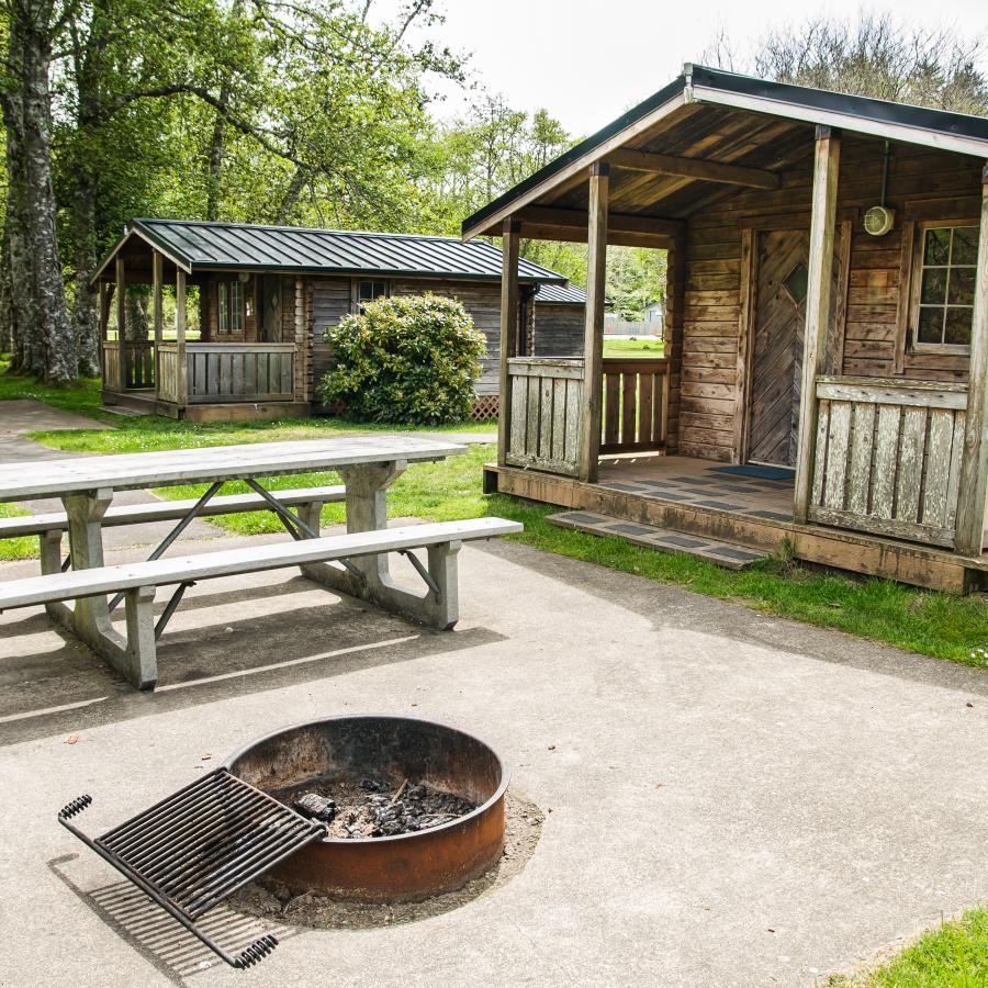 A cabin at Cape Disappointment that has a bench table and a fire pit out front