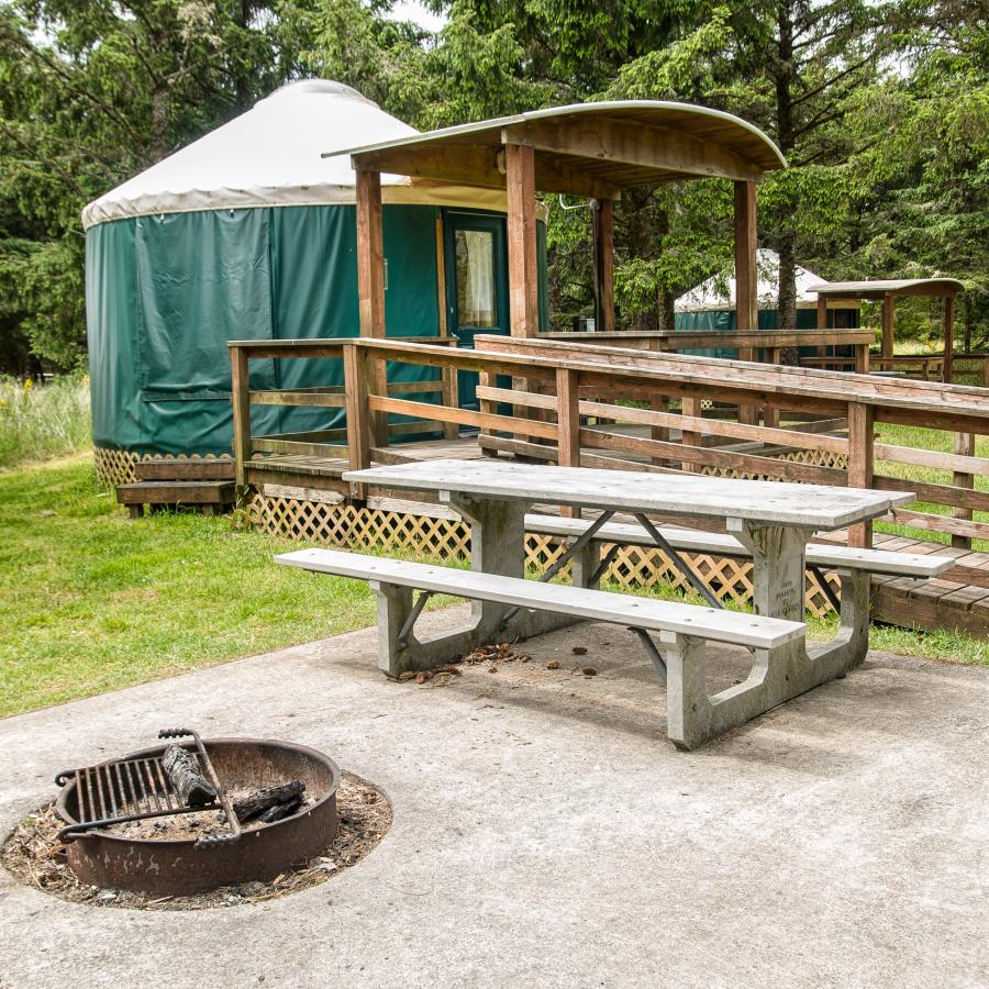 A Yurt with a ramp at Cape Disappointment accompanied with a picnic table and fire pit.