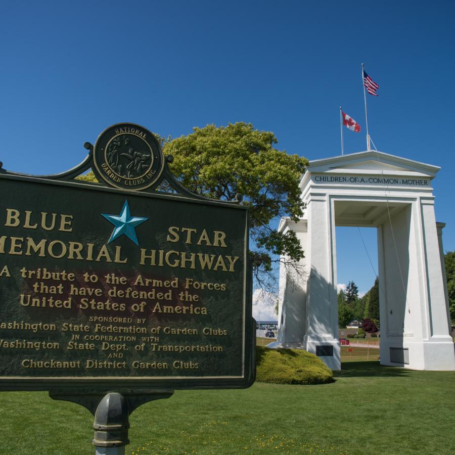 Memorial Sign in the park with the white Arch in the background on a blue sky sunny day