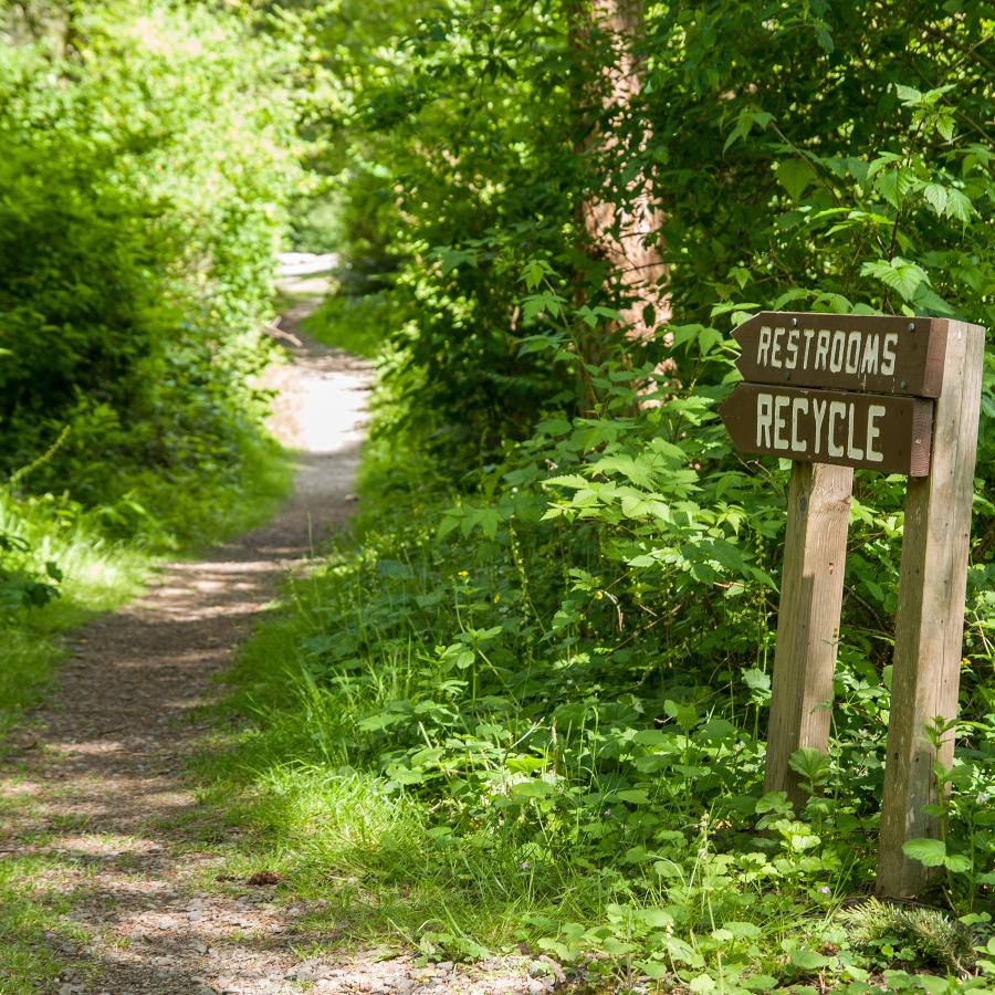 A restroom and recycle sign pointing to the trail.