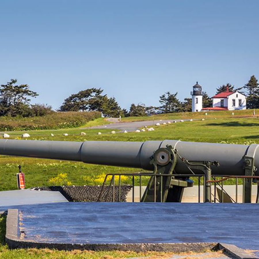 Large historical gun with lighthouse in the background on a sunny blue sky day