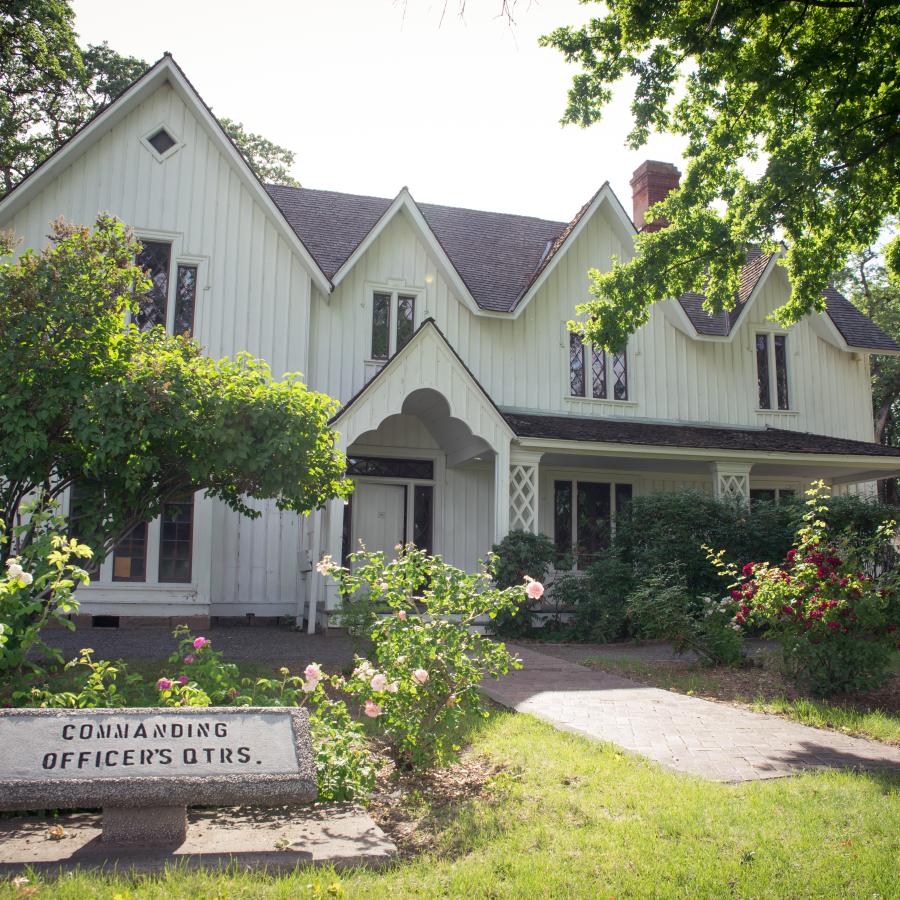 White commander's house behind blooming rose bushes.