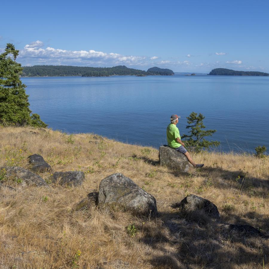 A visitor sitting on a rock enjoying the view of Hood Canal.