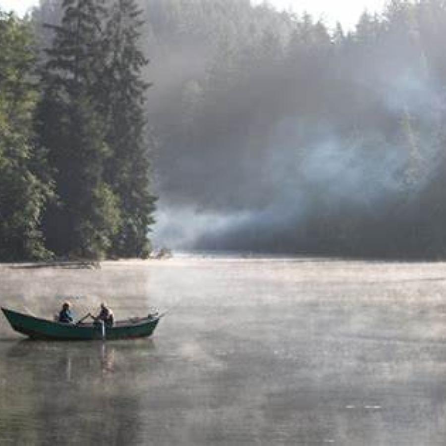 early morning fog on smooth lake with boat containing two people