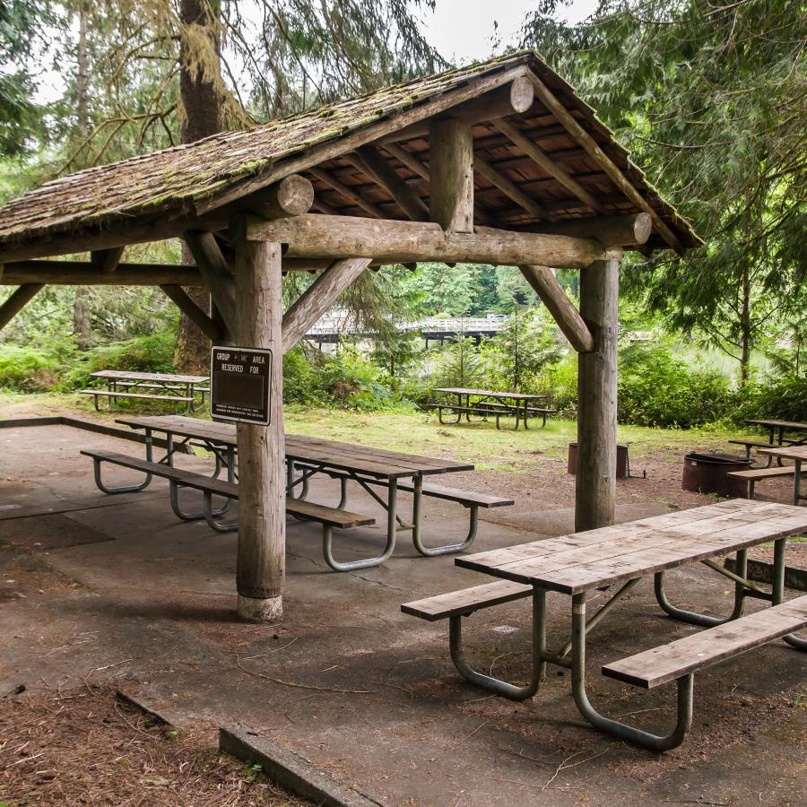 picnic shelter of round post wood beams with concrete pad and many picnic tables