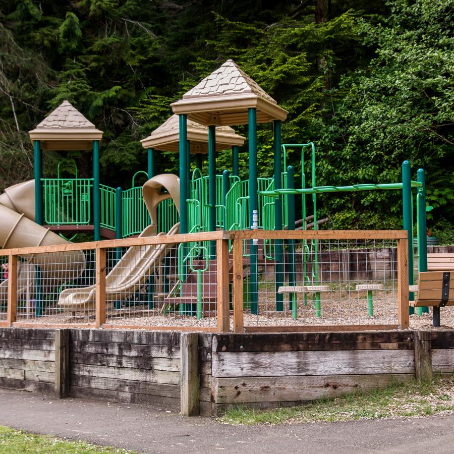large green and tan children's playground with protective fence surrounding