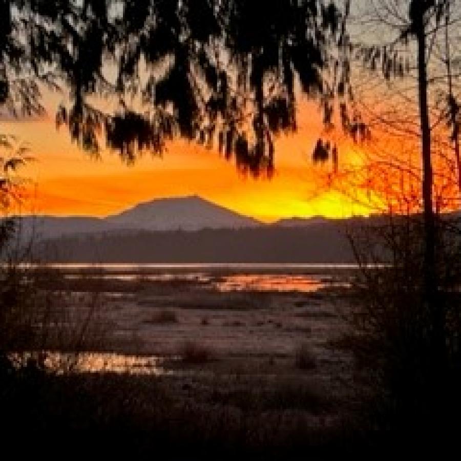 Mt Saint Helens Mountain at Sunrise with bright orange sky and yellow sun stretching up over the horizon