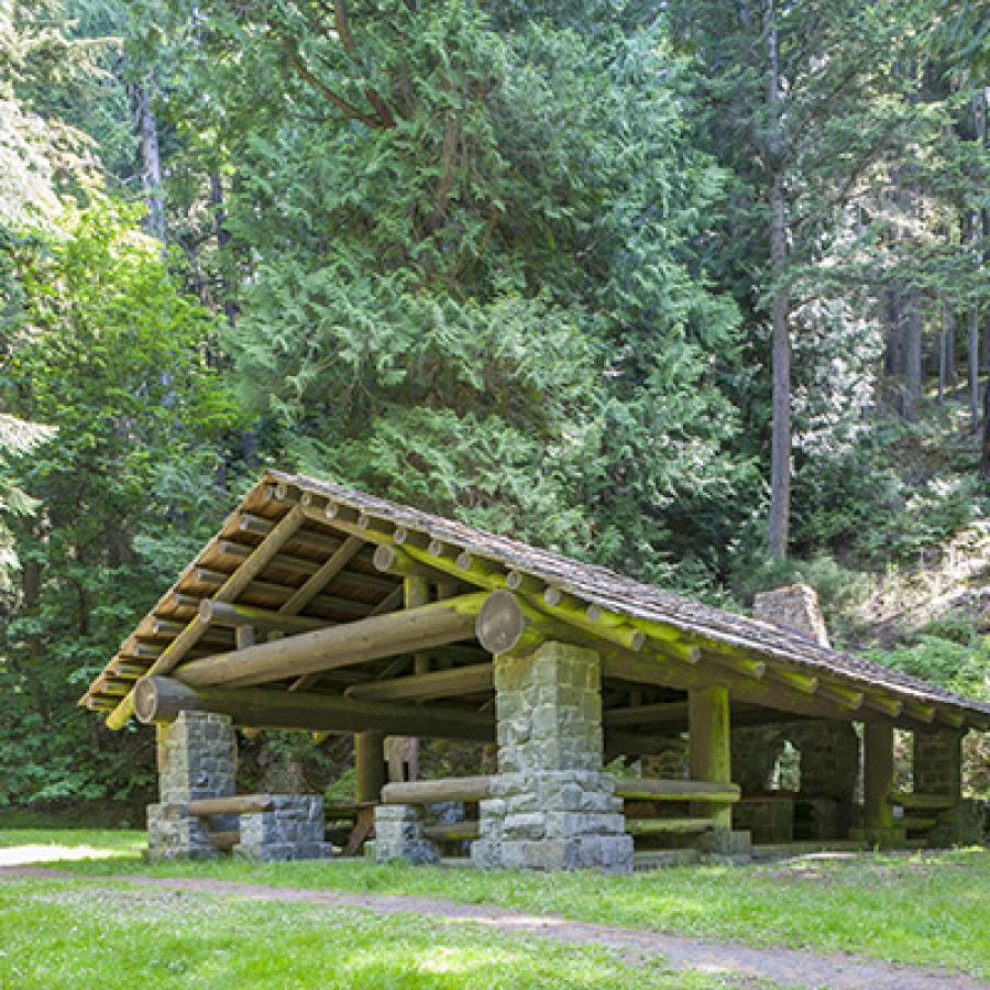 sheltered picnic area made of stone and logs surrounded by forest