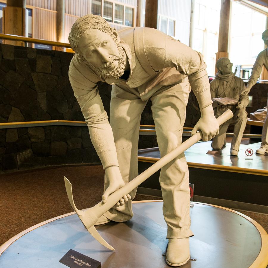 statue historical man using an axe to dig up earths surface