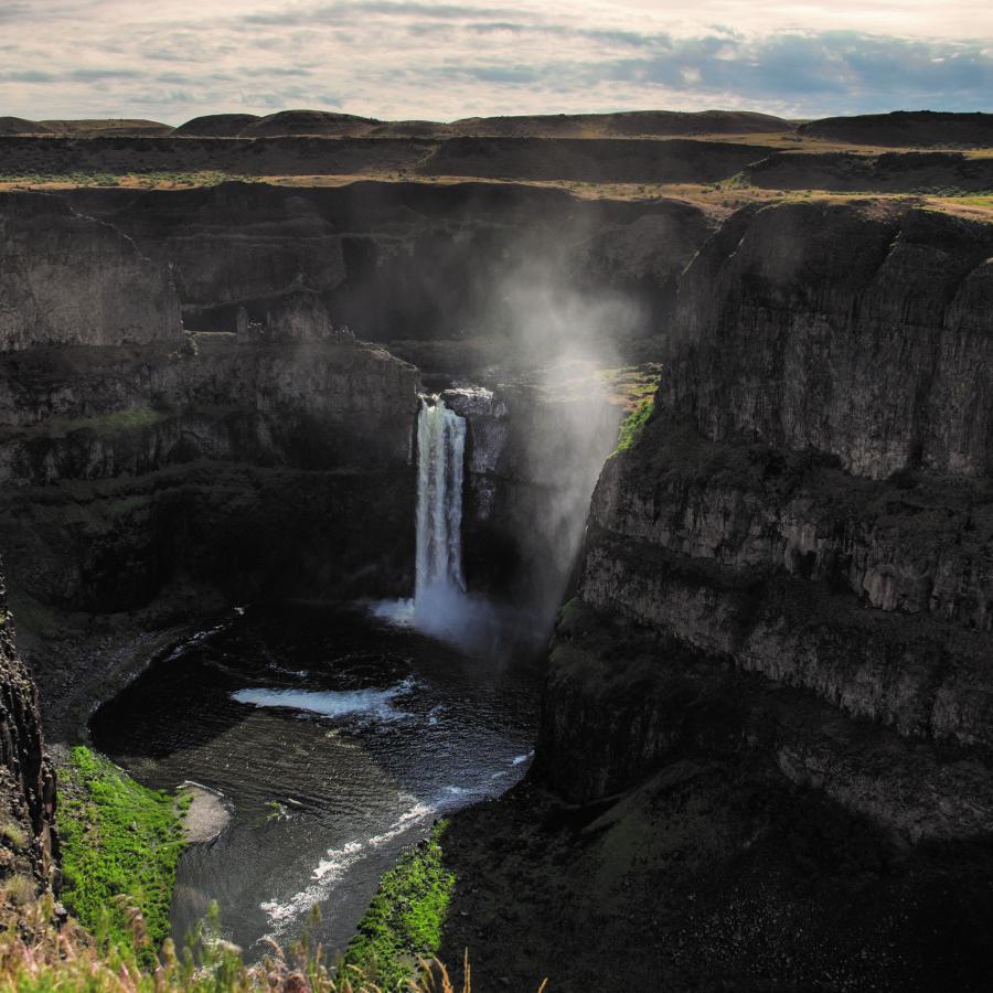 A waterfall at the end of a deep canyon with mist rising from the water below.