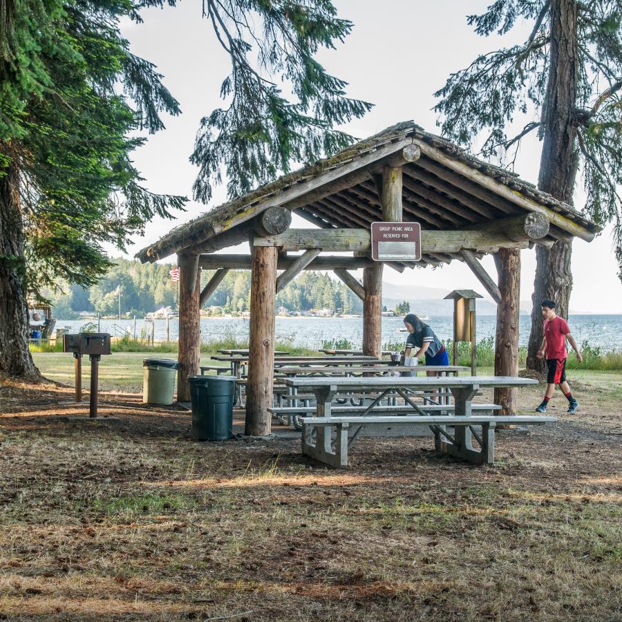 round log picnic shelter with tables , bbq grill and trash cans 