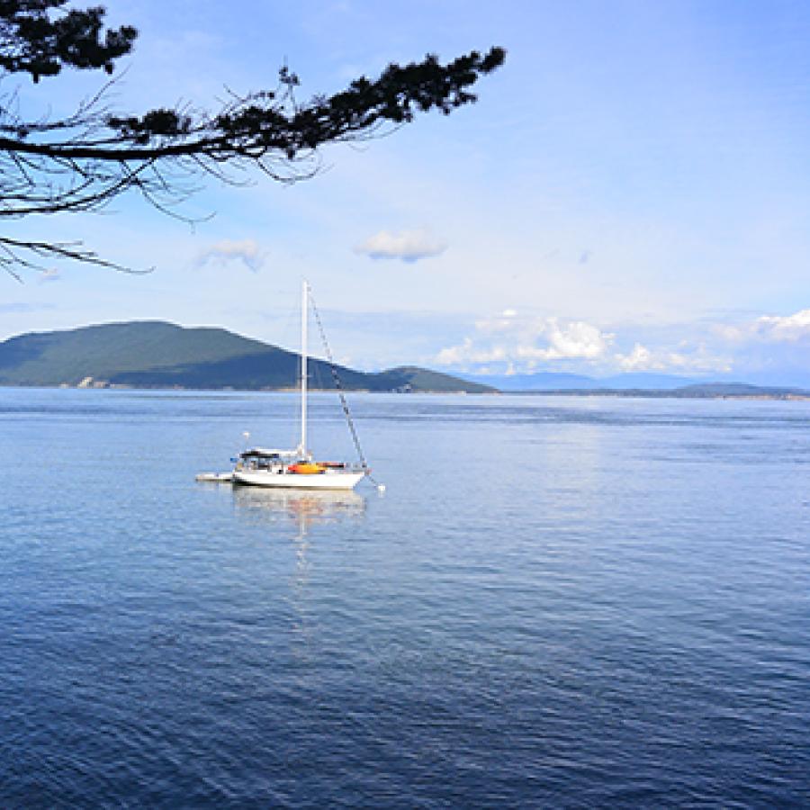 A boat is anchored off the coast of James Island and the green mountains of a nearby island are in the distance.
