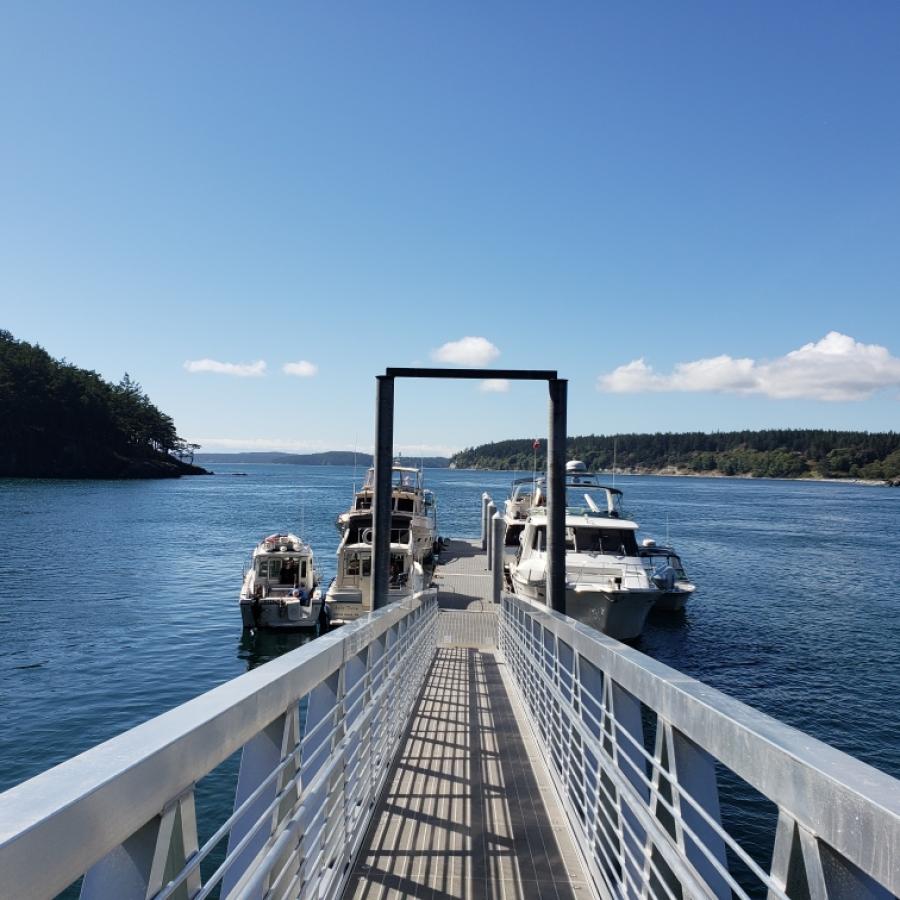 Looking down the dock at James Island. There are boats moored on either side. It is sunny and there are green islands in the distance.