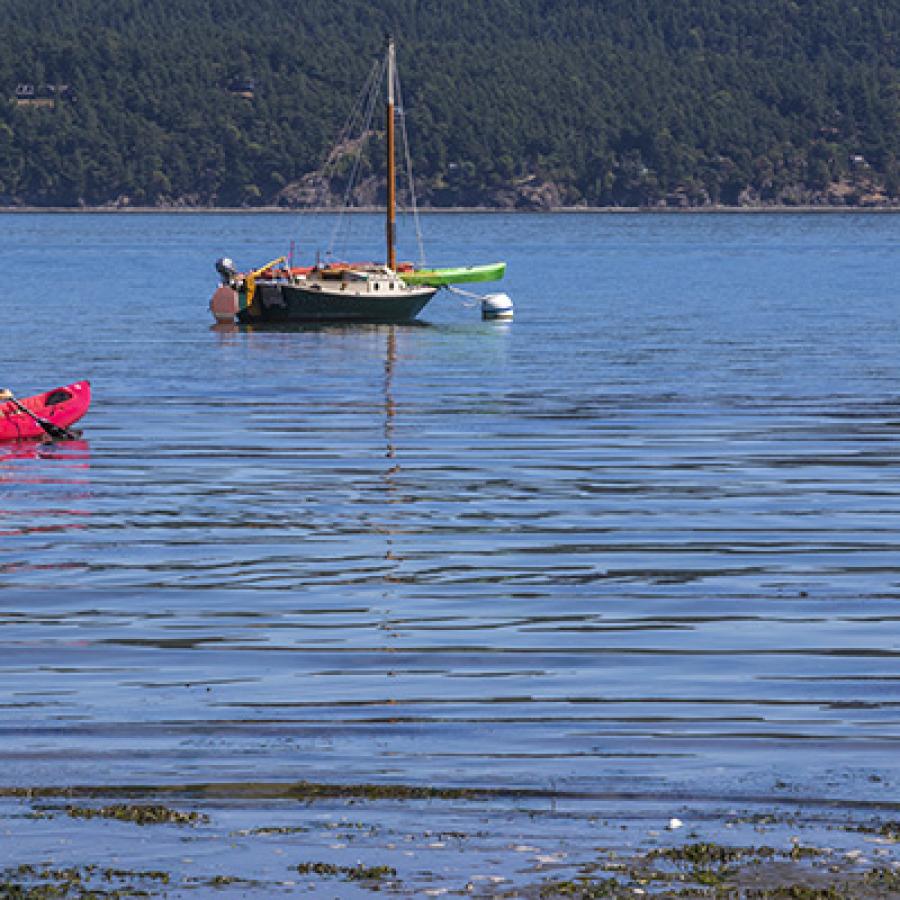 A kayaker paddles in the water and is heading toward a small boat moored nearby.